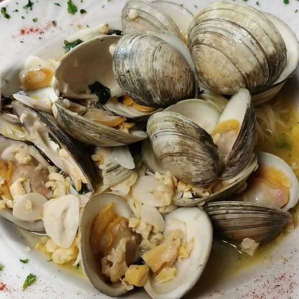Mama Nina's steamed clams in a white wine garlic sauce, garnished with parsley and spices.