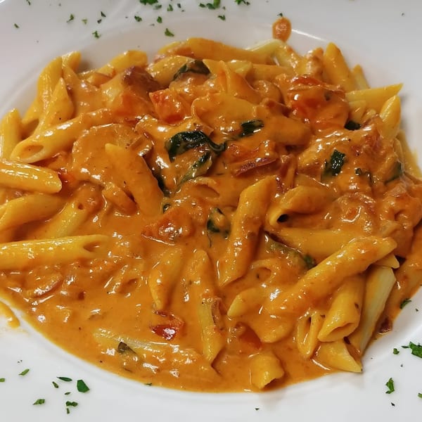 Penne pasta in a creamy orange sauce with chicken and spinach, garnished with parsley.