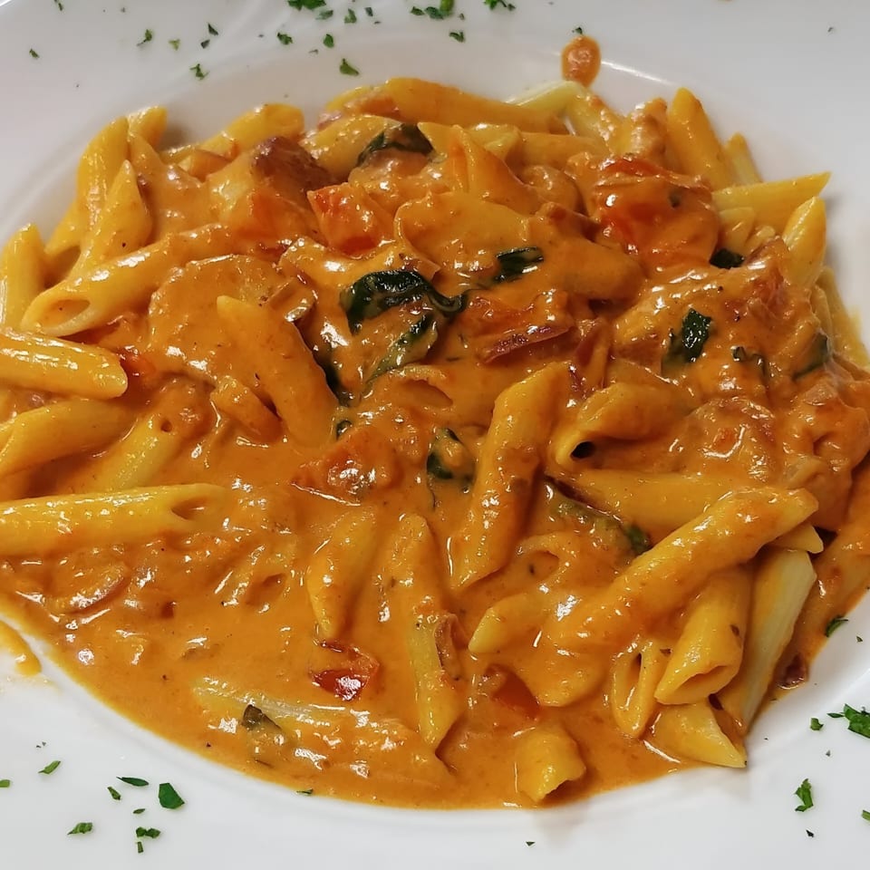 Penne pasta in a creamy orange sauce with chicken and spinach, garnished with parsley.